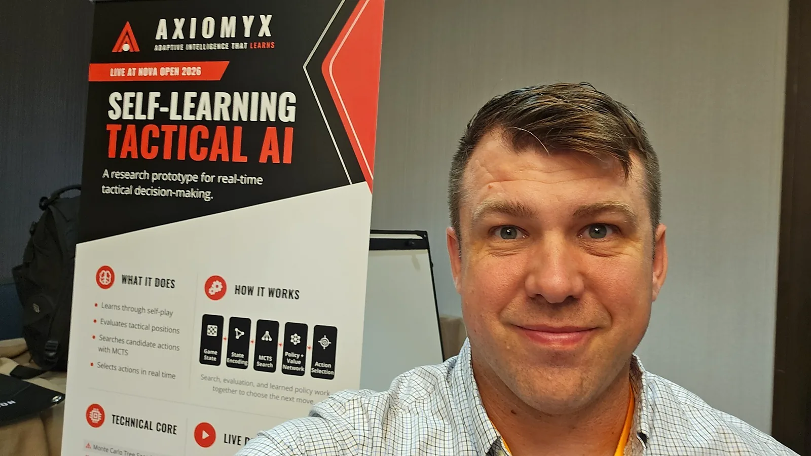 Raymond Fain at the Axiomyx stand, beside the Self-Learning Tactical AI banner.