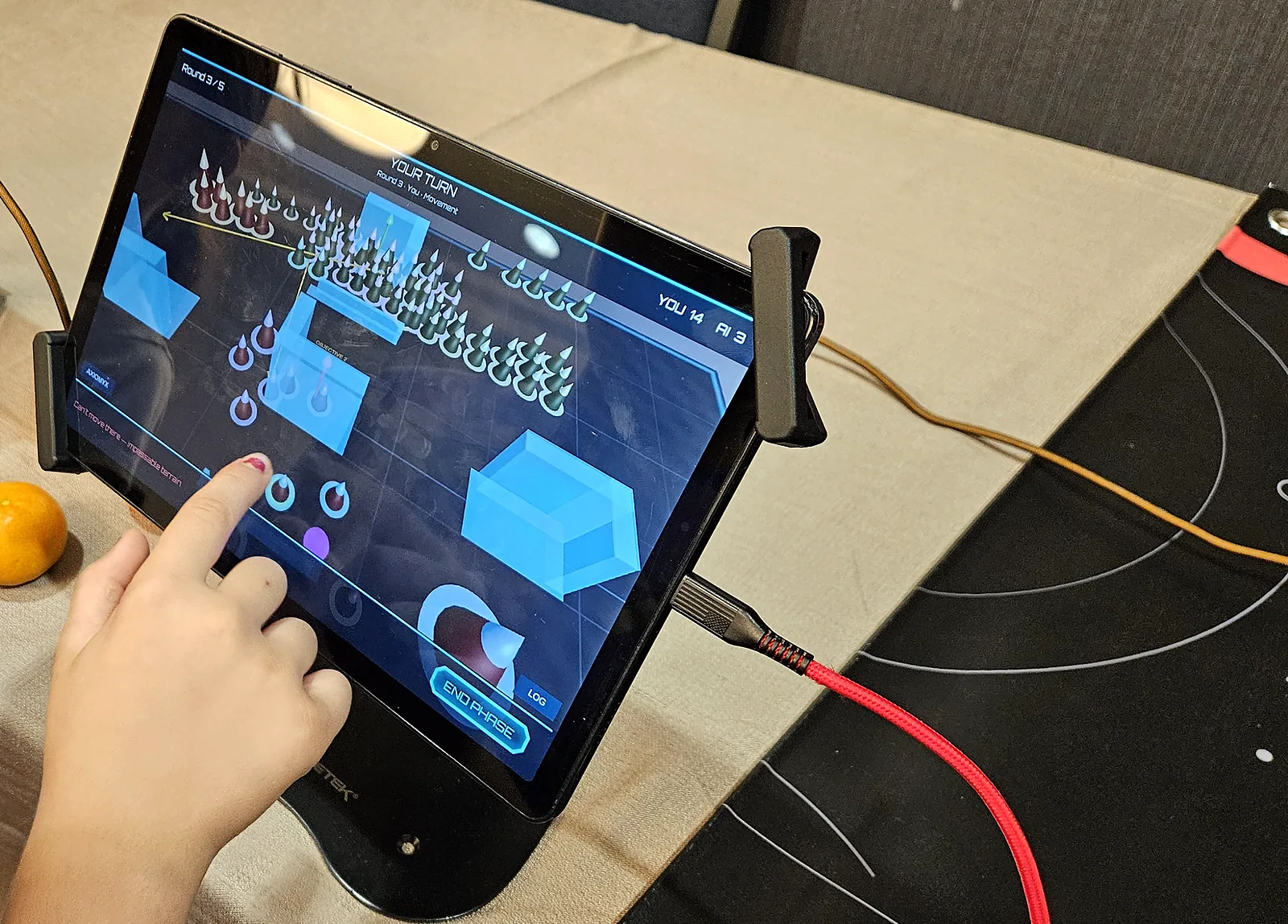 The Axiomyx tablet interface during a match, showing the board state, the round and phase, the running score and the end phase control.